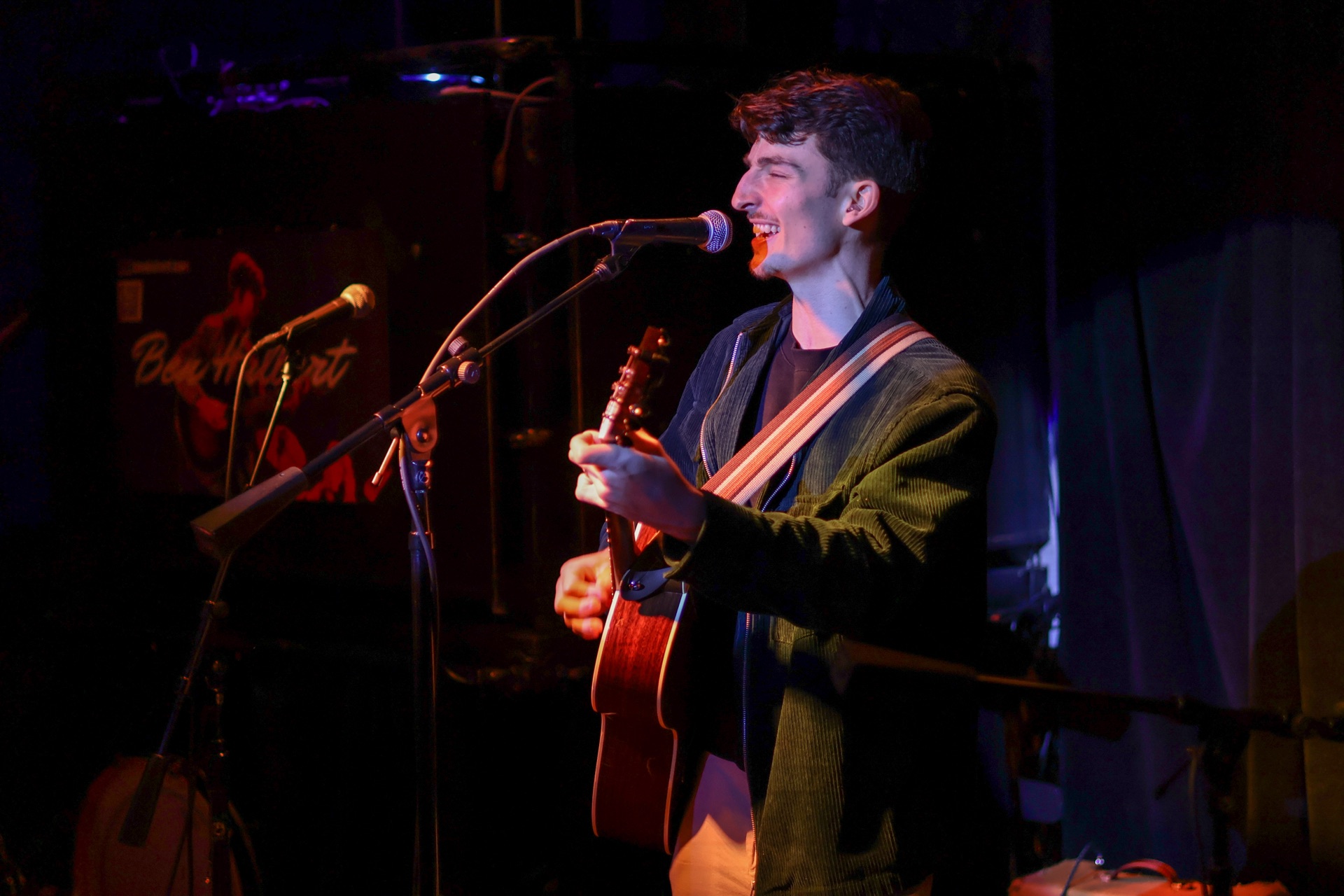 Ben Hulbert smiling as he performs on acoustic guitar